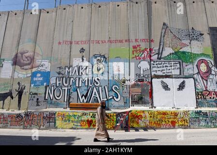 Bethlehem, West Bank. 23 Dez, 2019. Eine palästinensische Wanderungen vorbei an einem Abschnitt von Israels Trennmauer in der biblischen Stadt Bethlehem, West Bank, am Montag, 23. Dezember 2019. Eine neue Art der Arbeit mit der Überschrift "Auto von Bethlehem" durch Graffiti Künstler Banksy, zeigt eine Krippe vor dem israelischen Trennungsmauer, ist an seinem Walled-Off Hotels in der Nähe angezeigt. Foto von Debbie Hill/UPI Quelle: UPI/Alamy leben Nachrichten Stockfoto