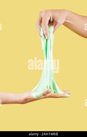 Hände von Menschen stretching Kalk Farbe SCHLEIM vor gelbem Hintergrund Stockfoto