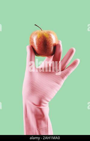 Behandschuhte hand Hausfrau halten frische reife roten Apfel, isoliert auf Grün Stockfoto