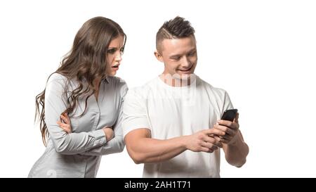 Portrait von Paar. Mann zu sein Telefon suchen. Wütend, verärgert Frau mit verschränkten Armen und schaut über die Schulter bei seinem Telefon isoliert auf weißem backgr Stockfoto