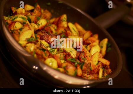 Kartoffeln gebraten mit Fleisch und Kräuter in eine glänzende Pfanne vor einem dunklen Hintergrund. Stockfoto