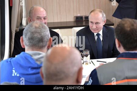 Taman, Russland. 23. Dezember, 2019. Der russische Präsident Wladimir Putin, rechts, erfüllt der Arbeitnehmer beim Reiten auf der neu eröffneten Eisenbahn auf der Krim-Brücke über die Straße von Kertsch verbinden auf der Krim, Krasnodar Dezember 23, 2019 in Taman, Russland. Die 19 km lange Brücke ist die längste in Europa und war fünf Jahre nach Russland im Anhang das Schwarze Meer Halbinsel. Credit: Aleksey Nikolskyi/Kreml Pool/Alamy leben Nachrichten Stockfoto