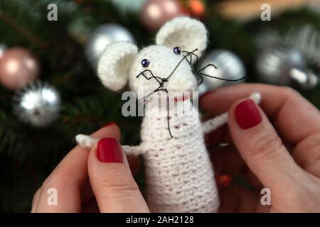 Handarbeit häkeln Spielzeug. Oder weiße Ratte Spielzeug in die Hände auf dem Hintergrund der Weihnachtsbaum. Weihnachten Ratte ist ein Symbol für das neue Jahr 2020. Stockfoto