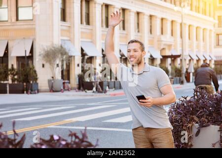 Weißer Mann mit einem Lächeln fordert ein uber-Treiber, während sein Handy in der Stadt auf einem hellen Tag Stockfoto