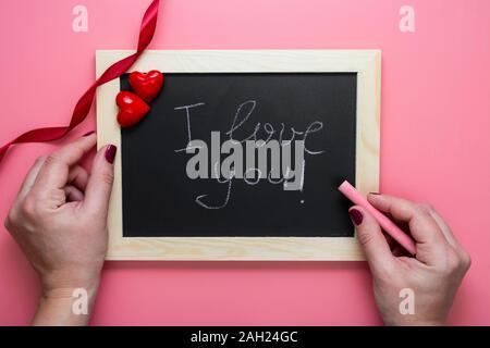 Valentinstag Hintergrund. Weibliche Hände schreib ich liebe dich Nachricht am Schwarzen Brett frame, Herzen und Red Ribbon, flach Mock up mit Kopie Raum Stockfoto