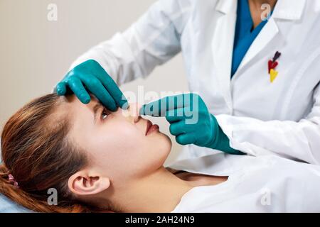Dame mit Pflaster auf der Nase, Arzt Patienten Prüfung Gesicht nach der plastischen Chirurgie. Stockfoto