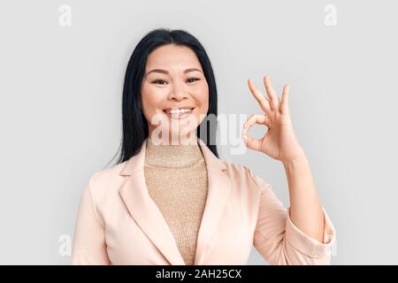 Freestyle. Asiatische geschäftsfrau stehen auf weißen angezeigt ok isoliert in die Kamera lächelt Fröhlich close-up Stockfoto