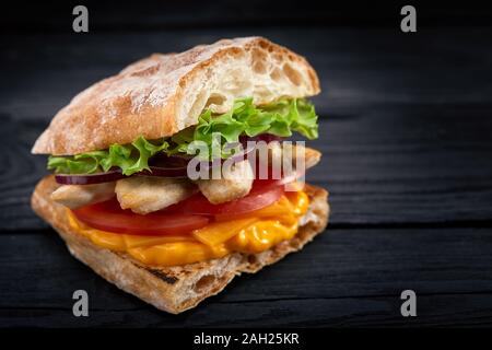 Appetitlich Sandwich auf einem Holzbrett. Baguette Sandwich mit Füllung aus Kopfsalat, Scheiben Tomate. Dunklen Hintergrund. Blick von oben. Close-up. Stockfoto