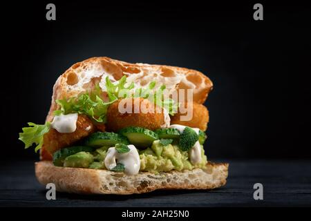 Appetitlich Sandwich auf einem Holzbrett. Baguette Sandwich mit Füllung aus Kopfsalat, Scheiben Tomate. Dunklen Hintergrund. Blick von oben. Close-up. Stockfoto