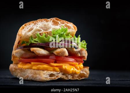 Appetitlich Sandwich auf einem Holzbrett. Baguette Sandwich mit Füllung aus Kopfsalat, Scheiben Tomate. Dunklen Hintergrund. Blick von oben. Close-up. Stockfoto