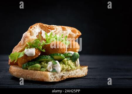 Appetitlich Sandwich auf einem Holzbrett. Baguette Sandwich mit Füllung aus Kopfsalat, Scheiben Tomate. Dunklen Hintergrund. Blick von oben. Close-up. Stockfoto