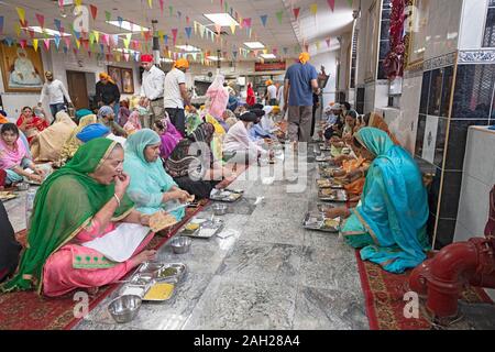 Sikh Frauen & Männer essen in einem langar, eine kostenlose Gemeinschaftsküche, an einem Tempel in South Richmond Hill, Queens, New York City. Stockfoto