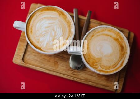 Ansicht von oben Bild Tasse heißen Cappuccino und Latte Art im Cafe auf dem roten Tisch und rustikalen Holzmöbeln zu schließen. Bis Tassen starken Kaffee mit schönen Schaum stand Stockfoto