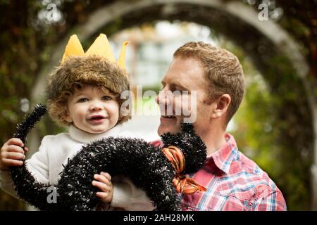 Lächelnd Mitte der erwachsene Mann seinen jungen Sohn in einem Halloween kostüm Holding. Stockfoto