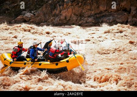Gruppe von Freunden White Water Rafting gemeinsam durch Stromschnellen in einem schnell fließenden Fluss. Stockfoto