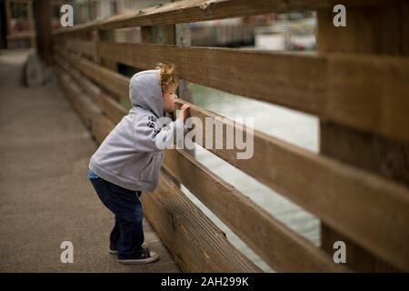 Neugierige kleine Junge spähen durch einen Zaun an der Waterfront Stockfoto