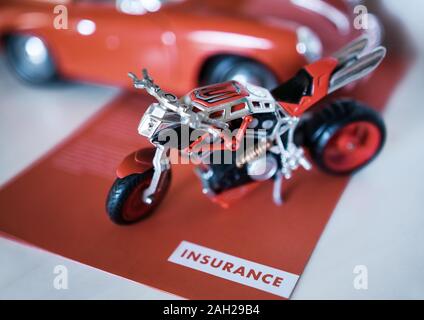 Ein Motorrad Spielzeug geparkt auf einem Versicherung Flyer, neben einem Auto. Stockfoto