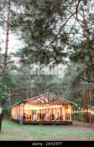 Verschwommenes Foto von hölzernen Hütte Restaurant mit Holztischen und -stühlen., mit Glühbirnen Vintage Design des Restaurants in den Wald in s eingerichtet Stockfoto