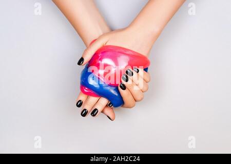 Hände mit schwarzen Maniküre holding Schleim in Blau und Rosa leuchtende Farben Stockfoto