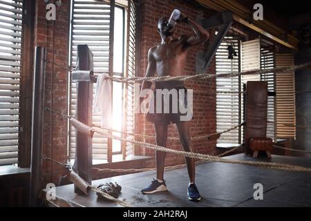 Afrikanische muskulösen Boxer Trinkwasser nach dem Sport Training beim Stehen auf Boxring in der Turnhalle Stockfoto