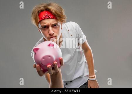 Portrait von stilvollen charmante blonde Kerl mit einem Sparschwein auf grauem Hintergrund. Stockfoto