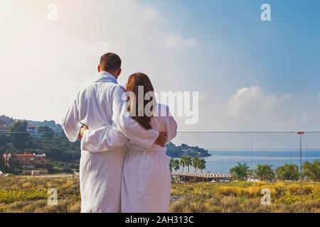 Mann und Frau paar In weißen Bademänteln stnding auf dem Balkon von Luxus Hotel und Blick auf das Meer. Honey Moon, Familienurlaub Konzept. Stockfoto