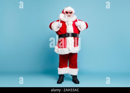 Volle Länge Körper Größe seiner Er schönen kühlen Heiter froh Fetten bärtigen Santa tragen warmen Wintermantel schauen Outfit mit zwei Doppel thumbup Stockfoto