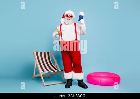 Volle Länge Körper Größe seiner er schön froh, heiter Fetten bärtigen Santa mit in den Händen Pass Tickets trinken Cocossaft über Blau isoliert Stockfoto