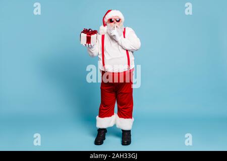 Volle Länge Foto lustige funky Fett moderne Santa Claus mit dicken Bauch zeigen Zeigefinger sprachlos Zeichen halten Geschenkbox möchten für Eve tragen rot geben Stockfoto