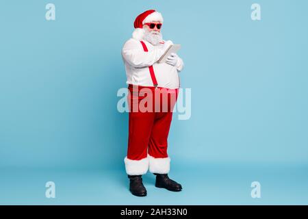 Volle Länge Foto lustige funky Fat santa claus Hippie Brillen mit großen Bauch Merkzettel plan im Notizbuch mit Stift Verschleiß schreiben Hosenträger Rot Stockfoto