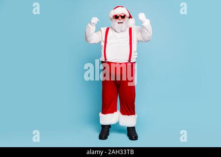 Volle Länge Foto von Fett lustig Santa Claus mit großen Bauch heben Fäuste ja das Gefühl der Stärke starke haben Weihnachtsfeier tragen rote Kappe Schrei Stockfoto