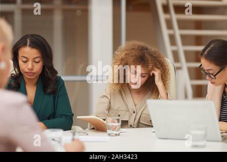 Horizontale Augenhöhe schoss der nachdenkliche junge Unternehmerinnen ihren Job zusammen sitzen am Tisch Stockfoto
