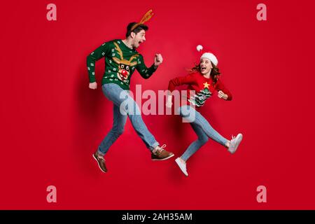 Voller Körper Foto von aufgeregt springen Paar hetzende für x-mas Rabatte tragen hässliche ornament Jumper isolierten roten Farbe Hintergrund Stockfoto