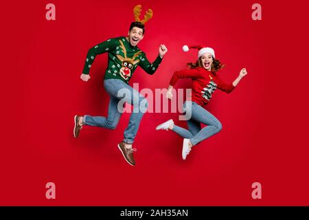 Volle Länge Foto von jumping Paar von x-mas Preise beeilen Kostüme kaufen tragen hässliche ornament Jumper isolierten roten Farbe Hintergrund begeistert Stockfoto