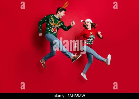 Volle Größe Foto von aufgeregt springen Paar schnell laufen für x-mas Rabatt shopping tragen hässliche ornament Jumper isolierten roten Farbe Hintergrund Stockfoto