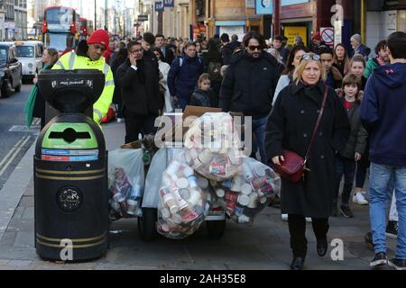 Käufer vorbei street Cleaner auf die geschäftige Oxford Street, als er Volle Abfallsäcke Leergut während des Urlaubs rush Am 23. Dezember 219 Stockfoto