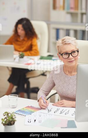 Fashion Designer sitzen an Ihrem Arbeitsplatz in modernen Büro Zimmer vertikale Portrait arbeiten Stockfoto