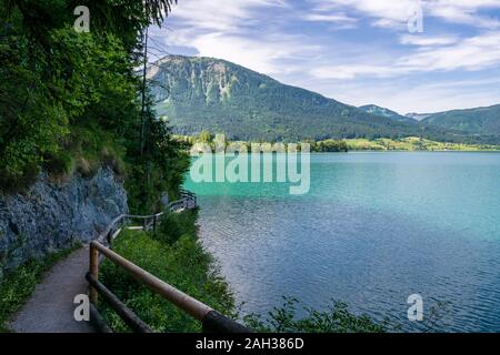 Steg am Rand der türkisfarbenen See namens Wolfgangsee Berge im Hintergrund und Wolken am Himmel Stockfoto