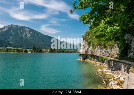 Steg am Rand der türkisfarbenen See namens Wolfgangsee Berge im Hintergrund und Wolken am Himmel Stockfoto