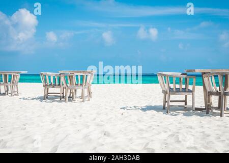 Stühle und Tische auf den weißen Strand der Malediven mit dem türkisblauen Meer im Hintergrund und Wolken am blauen Himmel Stockfoto