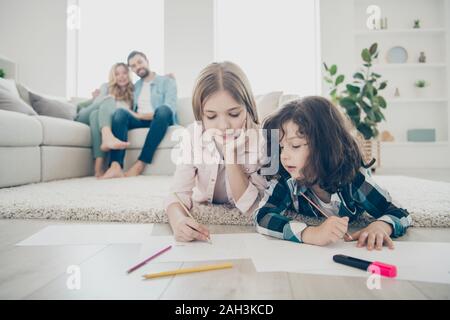 Foto von großen Familie zwei Kinder lügen, flauschigen Teppich, Zeichnungen, während die Eltern genießen Sie freundlich angenommene Kinder Stockfoto