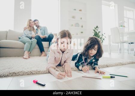 Foto von großen Familie zwei Kinder lügen, flauschigen Teppich, Zeichnungen, während die Eltern genießen Sie freundlich angenommene Kinder Stockfoto