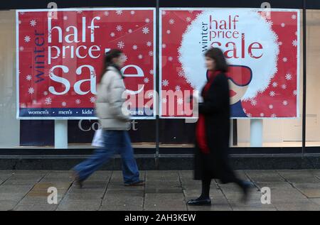 Weihnachtskäufer Spaziergang, vorbei an einem Verkauf Zeichen im Fenster der Debenhams auf Winchester High Street, wie Geschäfte für den Boxing Day Vertrieb vorbereiten. Stockfoto