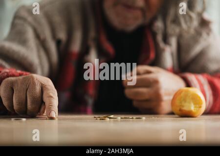 Low Angle View der älteren wohnungslosen Menschen zählen von Münzen mit einem gebissen Apple auf den Schreibtisch. Stockfoto