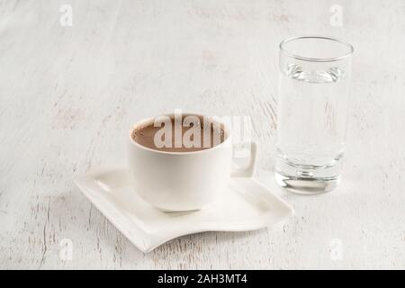 Türkischer Kaffee, serviert mit einem Glas Wasser auf einem Holztisch Stockfoto