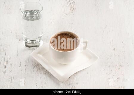 Türkischer Kaffee, serviert mit einem Glas Wasser auf einem Holztisch Stockfoto
