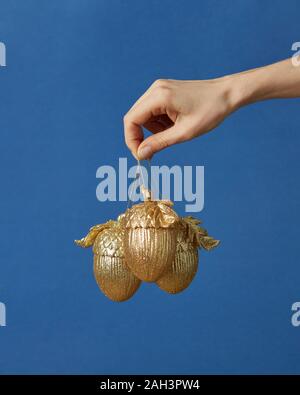 Weihnachtsdekoration goldenen Eicheln in einer Frau die Hand auf einem klassischen blauen Hintergrund mit kopieren. Stockfoto