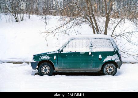 Eine alte verlassene kleine grüne Auto bedeckt mit Schnee gestreut. geparkt am Waldrand im Winter. Stockfoto