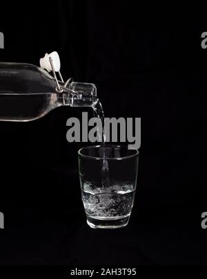 Das Gießen von Wasser aus der Flasche in ein Glas auf schwarzem Hintergrund Stockfoto
