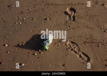 Menschliche Schuhe footprints neben Kunststoff Papierkorb auf den Strand gespült Stockfoto